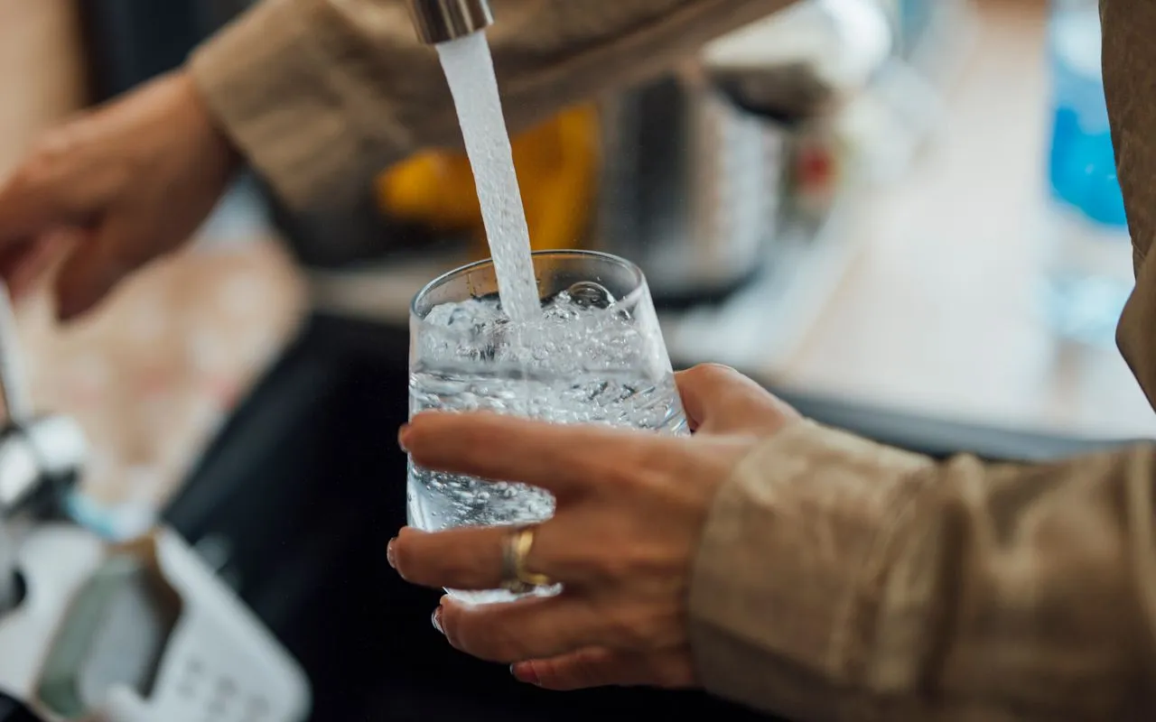 Person filling a drinking glass with water at a kitchen sink faucet
