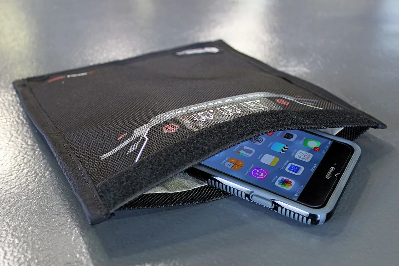 Smartphone being sealed inside a Mission Darkness faraday bag, with the metallic shielding fabric liner visible